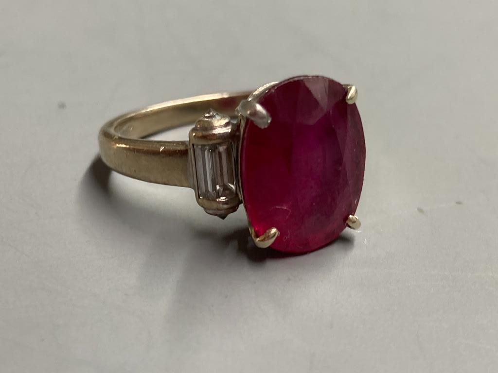 A modern yellow metal (stamped 750) and oval cut single stone ruby dress ring, with baguette cut diamond set shoulders